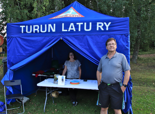Vastaanottopisteenä toimineen sinisen teltan sisällä Aini Rautanen ja teltan edessä Kari Iltanen.