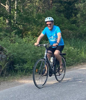 Mies ajaa polkupyörällä sininen paita päällä.