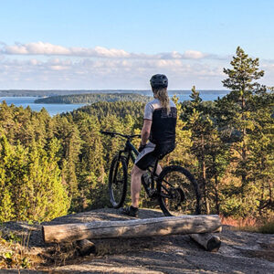 Maastopyöräilijä istuu pyörän päällä kalliolla ja katsoo merelle horisonttiin.