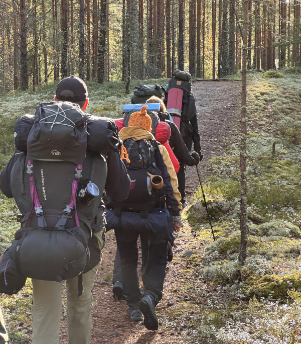 Ihmisiä patikoimassa rinkka selässä metsässä.