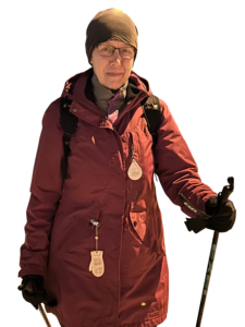 Nainen viininpunaisessa ulkoiluasussa kävelysauvat kädessä.